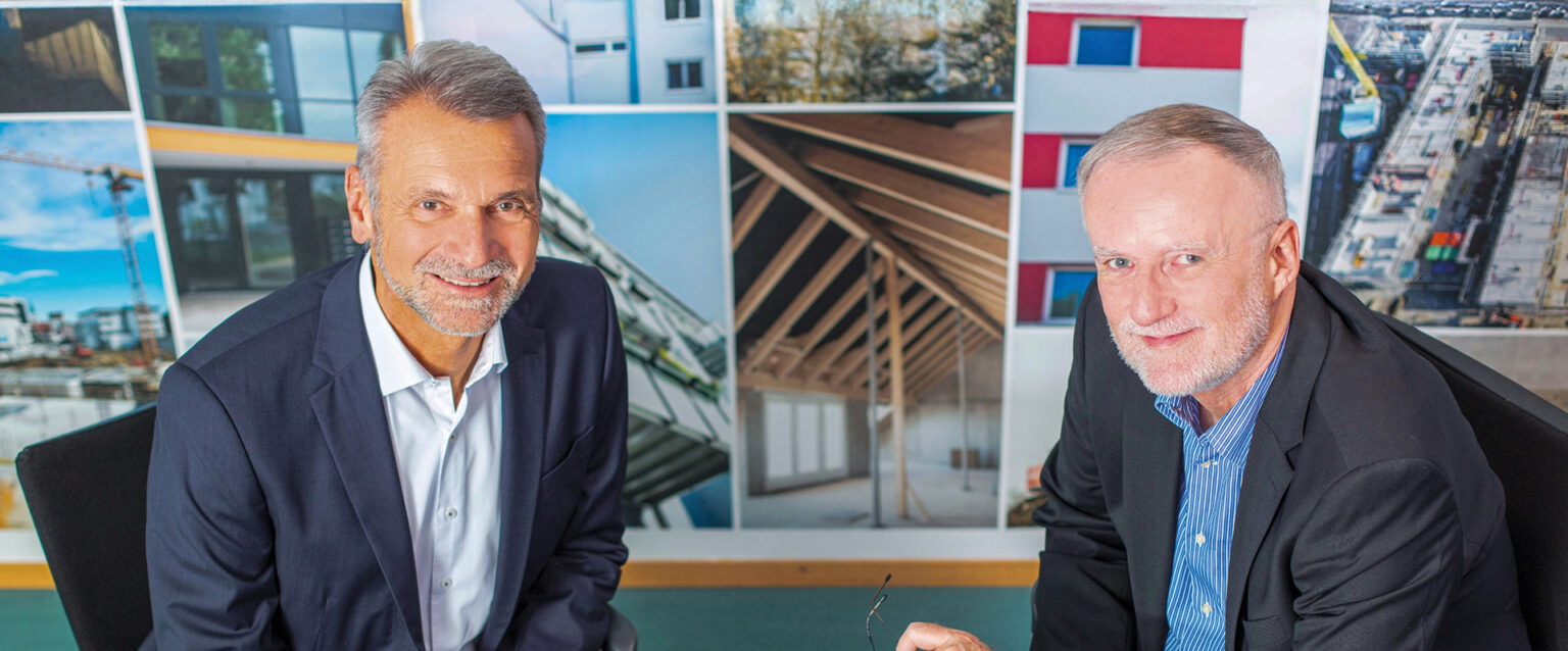 Die Vorstände der Familienheim Bodensee, Stefan Andelfinger und Marco Bächle, am Besprechungstisch vor Baustellenfotos