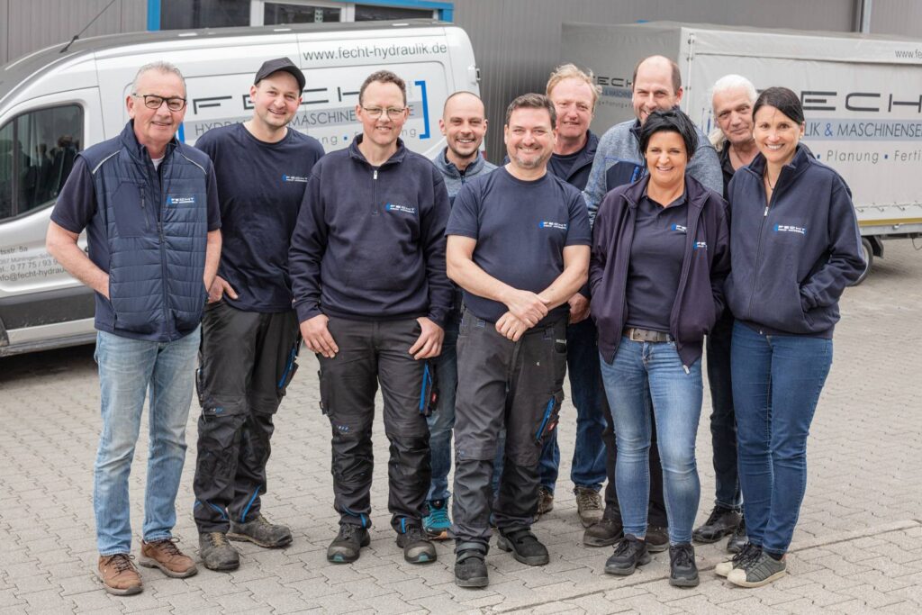 Das Team von Fecht Hydraulik vor Firmenfahrzeugen am Firmengebäude in Mühlingen