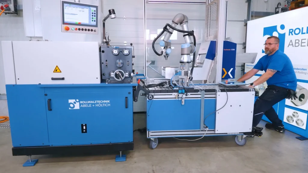Mitarbeiter schiebt das fahrbare Robotermodul von der Walzmaschine weg, damit sie von Hand bestückt werden kann
